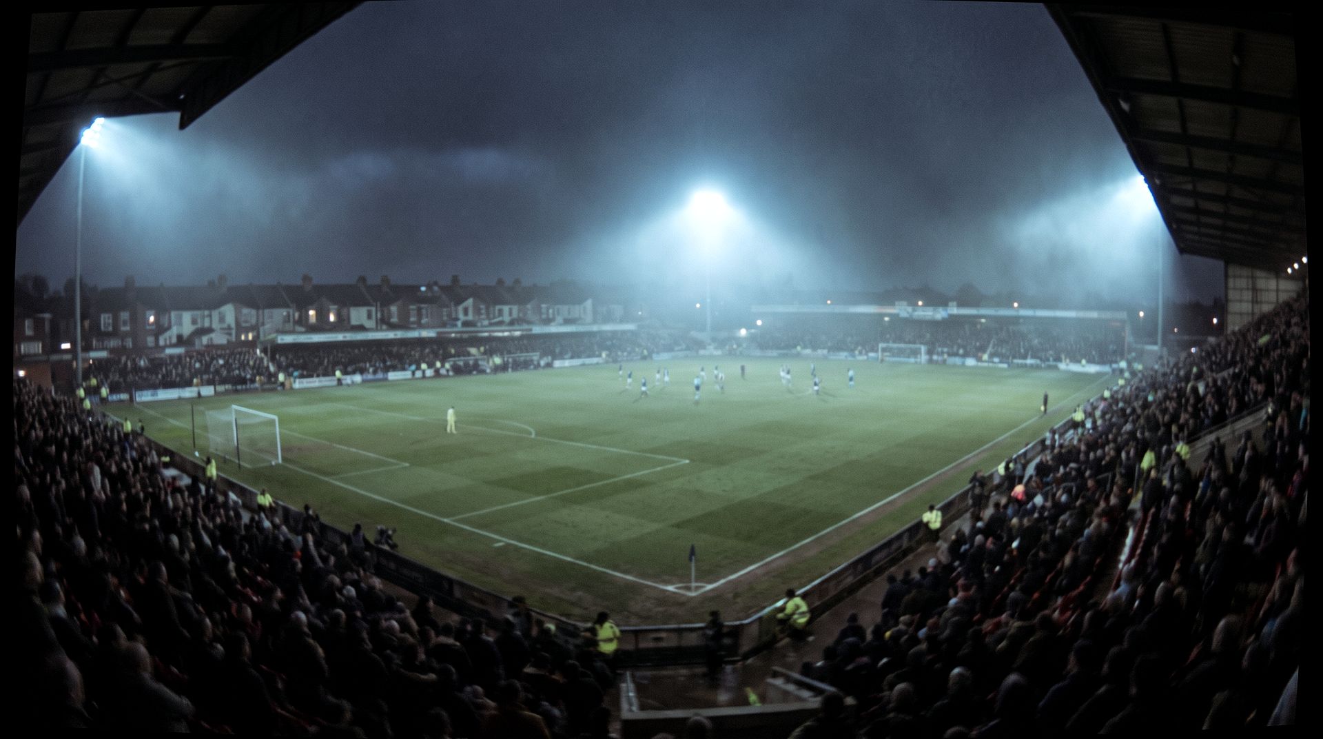 High camera view across a floodlit English football ground on a matchday evening