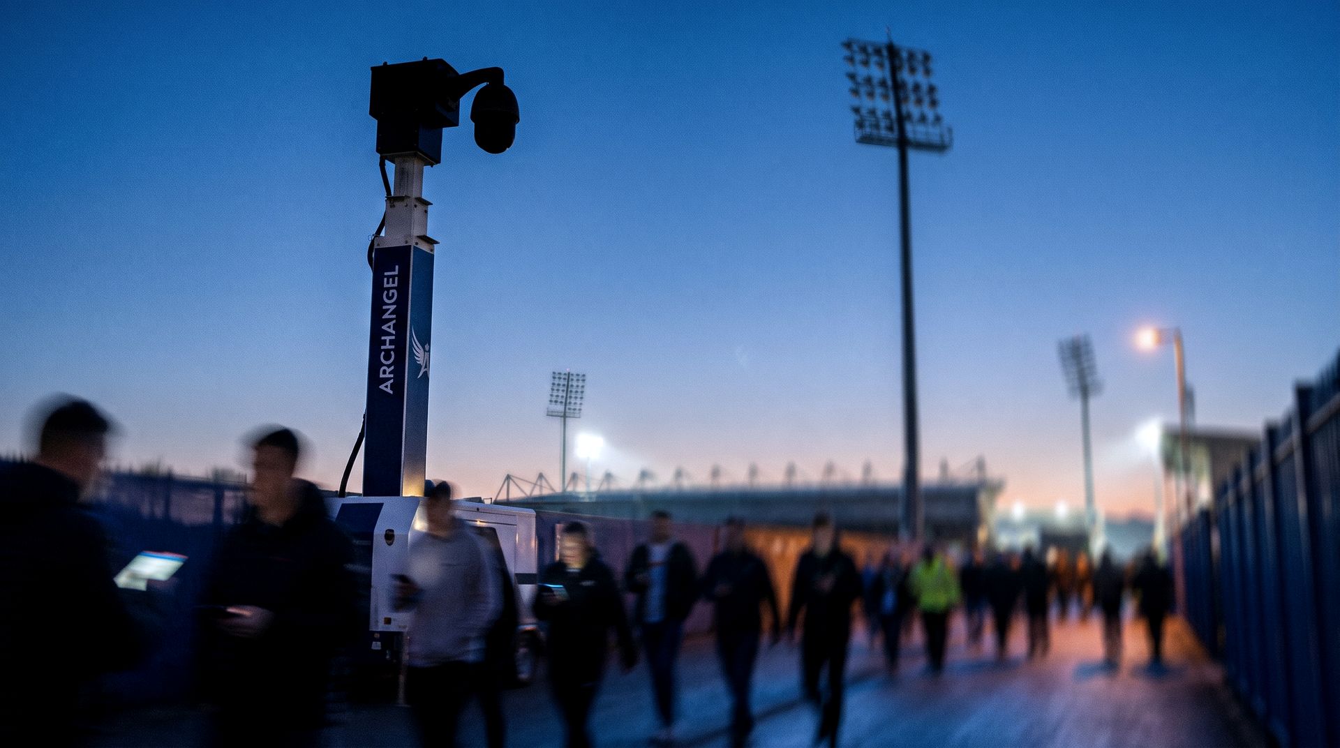 Archangel CCTV tower watching a stadium approach route as supporters walk in at dusk